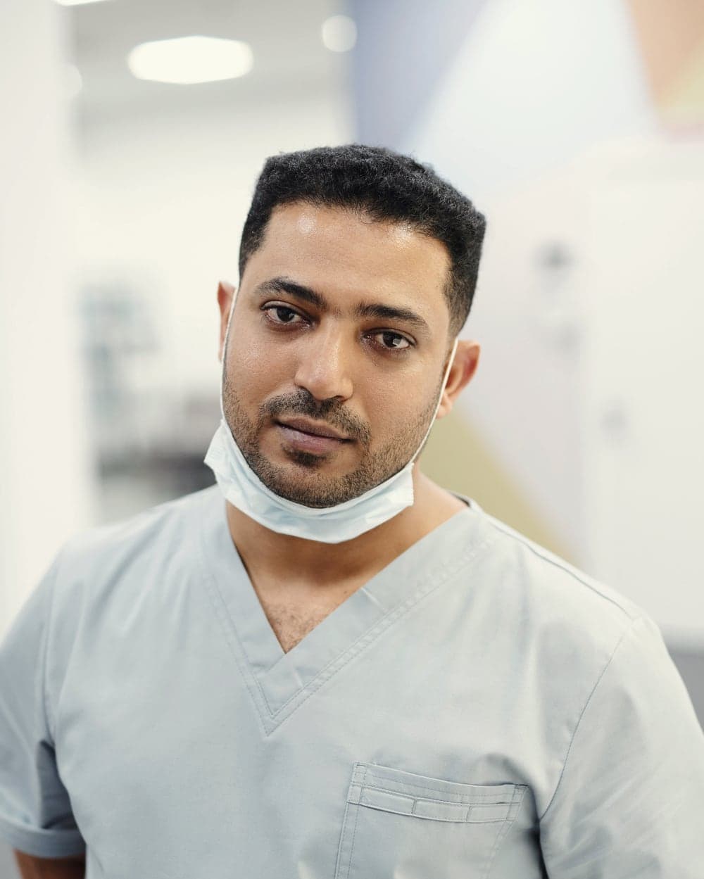 Portrait of Dr. Karthik Menon in light blue scrubs, mask lowered.