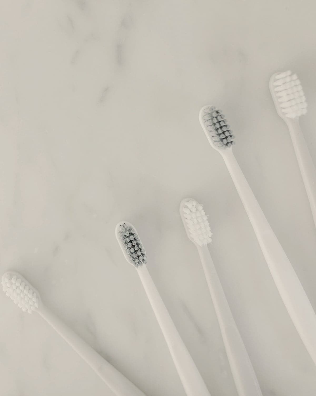Soft white toothbrushes laid out on pale marble.